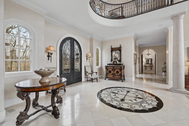 tiled foyer featuring decorative columns, ornamental molding, a high ceiling, and french doors