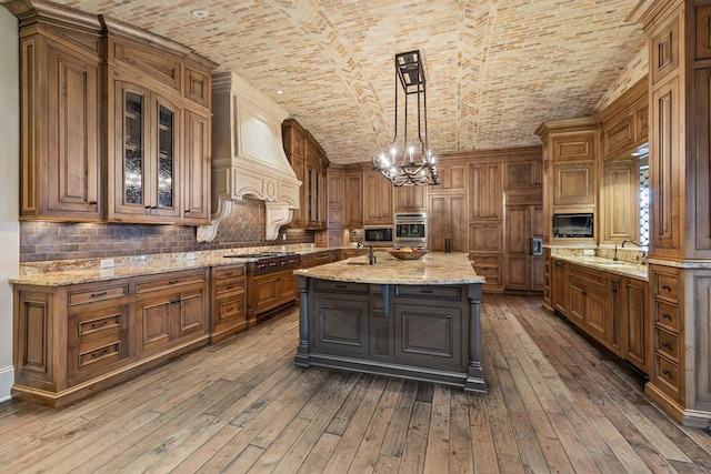 kitchen featuring brick ceiling, a kitchen island with sink, premium range hood, and decorative light fixtures