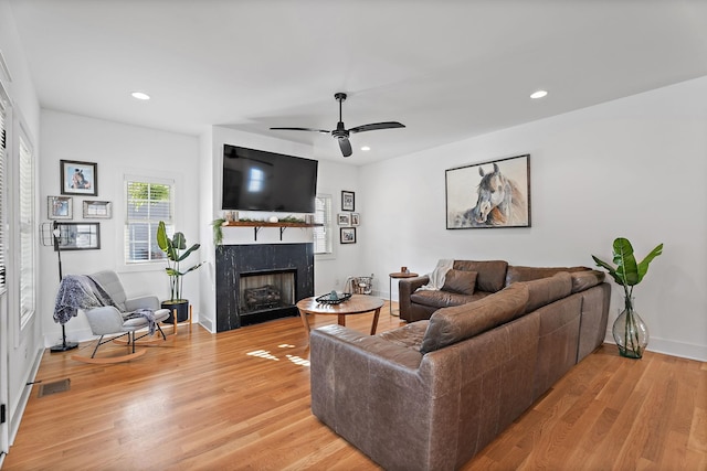 living room with ceiling fan, a premium fireplace, and light wood-type flooring