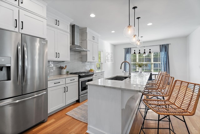 kitchen featuring a breakfast bar, a center island with sink, stainless steel appliances, light stone countertops, and wall chimney range hood