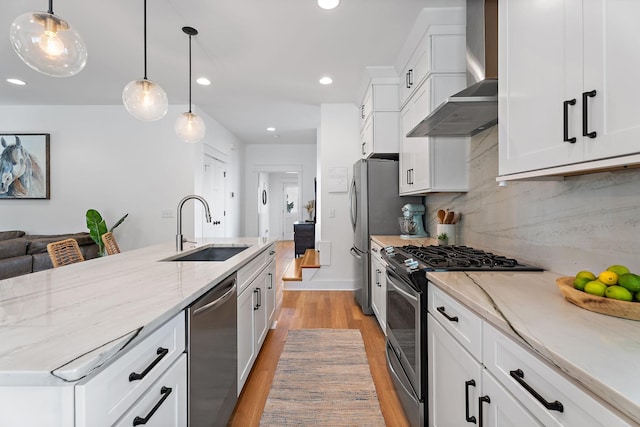 kitchen featuring sink, white cabinetry, hanging light fixtures, stainless steel appliances, and wall chimney exhaust hood