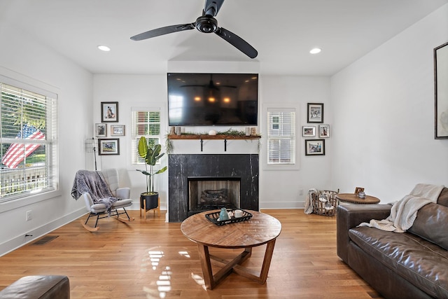 living room with a high end fireplace, ceiling fan, and light wood-type flooring