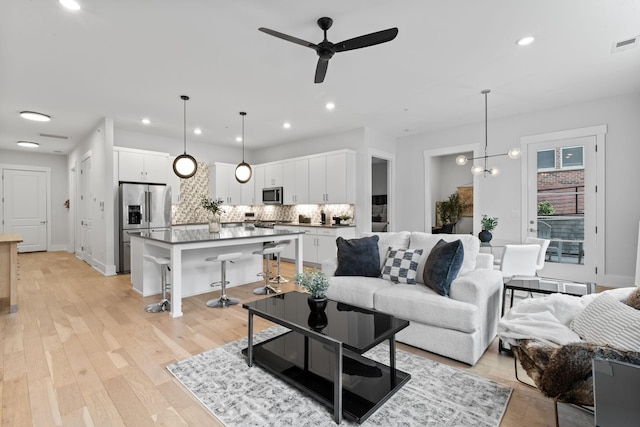 living room featuring ceiling fan with notable chandelier and light wood-type flooring