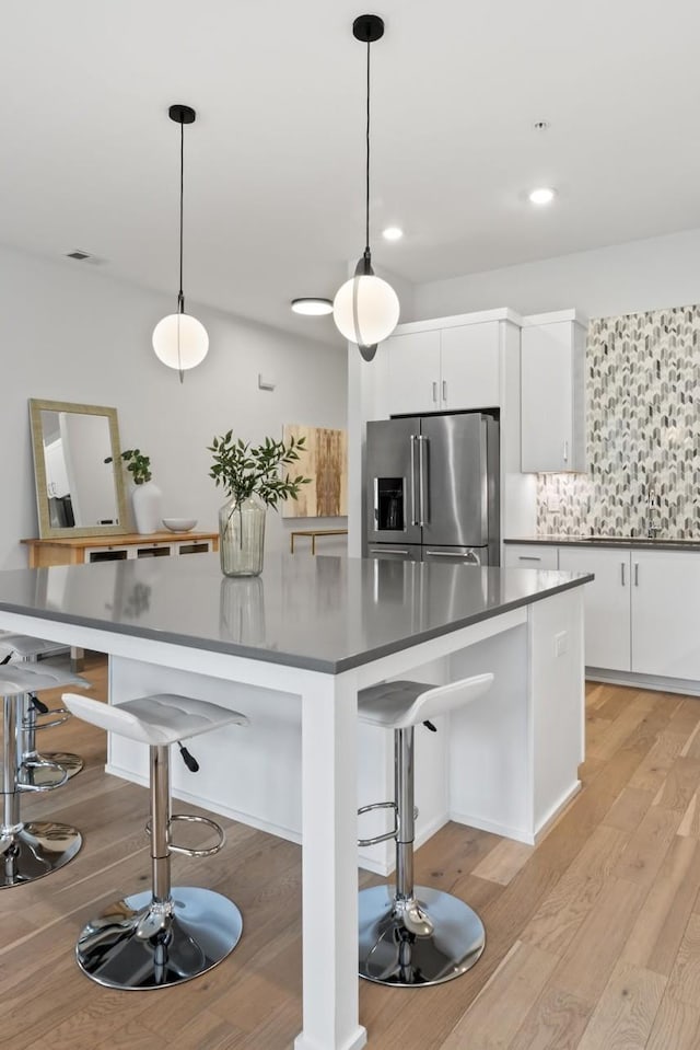 kitchen featuring high end fridge, hanging light fixtures, white cabinets, and a kitchen bar