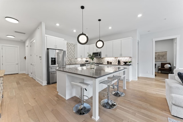 kitchen featuring appliances with stainless steel finishes, white cabinets, a kitchen breakfast bar, hanging light fixtures, and light hardwood / wood-style floors