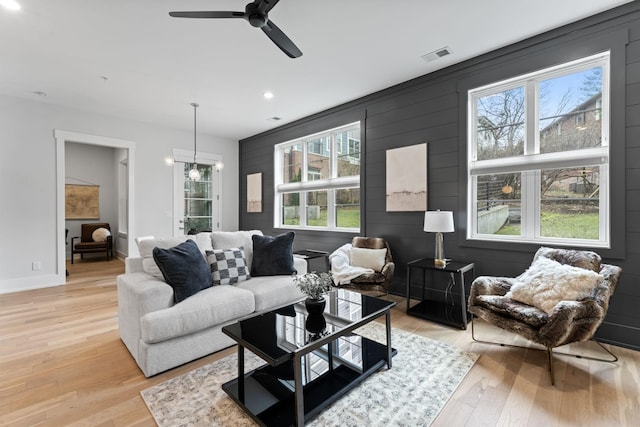 living room featuring ceiling fan with notable chandelier and light hardwood / wood-style flooring