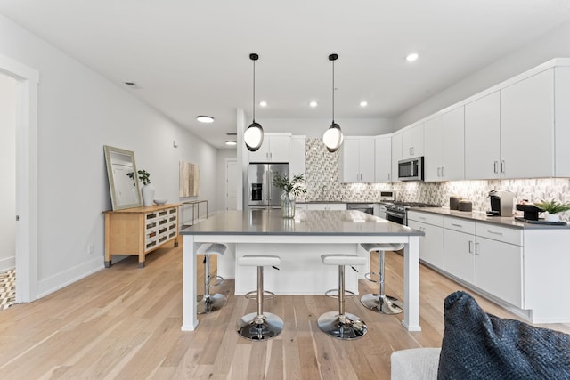 kitchen featuring decorative light fixtures, appliances with stainless steel finishes, an island with sink, decorative backsplash, and white cabinets