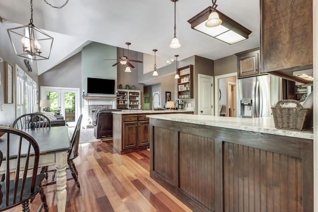 kitchen with light stone counters, wood-type flooring, high vaulted ceiling, stainless steel fridge, and kitchen peninsula