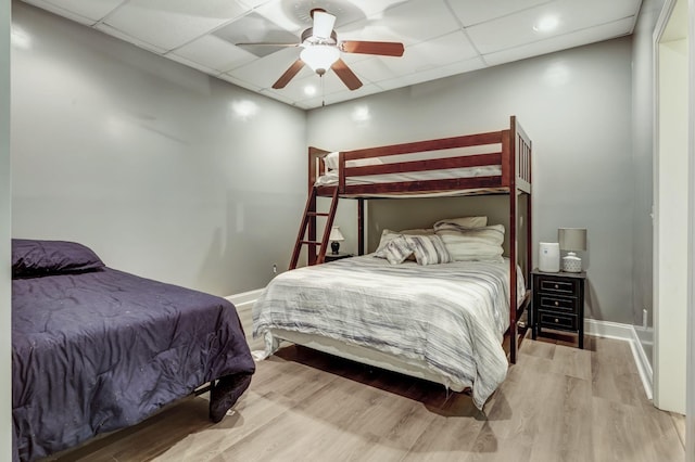 bedroom featuring a drop ceiling, wood-type flooring, and ceiling fan