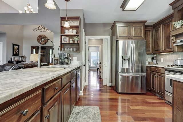 kitchen with appliances with stainless steel finishes, hanging light fixtures, backsplash, dark brown cabinetry, and dark hardwood / wood-style flooring