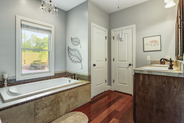 bathroom with hardwood / wood-style flooring, a notable chandelier, vanity, and tiled tub