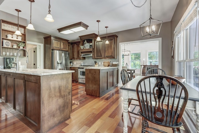 kitchen featuring sink, an inviting chandelier, hanging light fixtures, appliances with stainless steel finishes, and wall chimney range hood