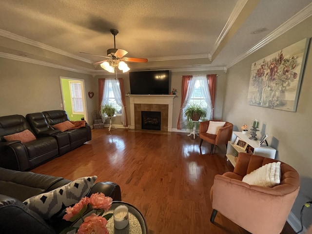 living room with a tile fireplace, wood-type flooring, ceiling fan, a raised ceiling, and crown molding