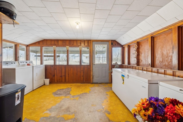 clothes washing area featuring wooden walls, washer and clothes dryer, and a wealth of natural light