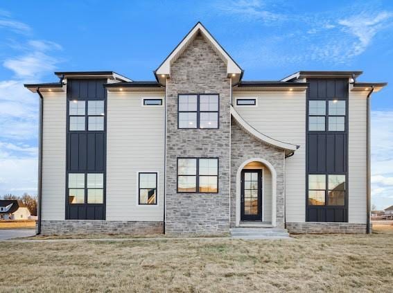 view of front of house featuring board and batten siding, a front yard, and stone siding