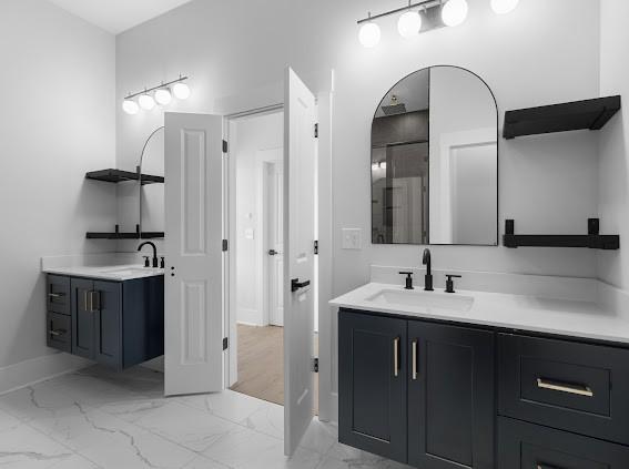 bathroom featuring marble finish floor, two vanities, a sink, and baseboards