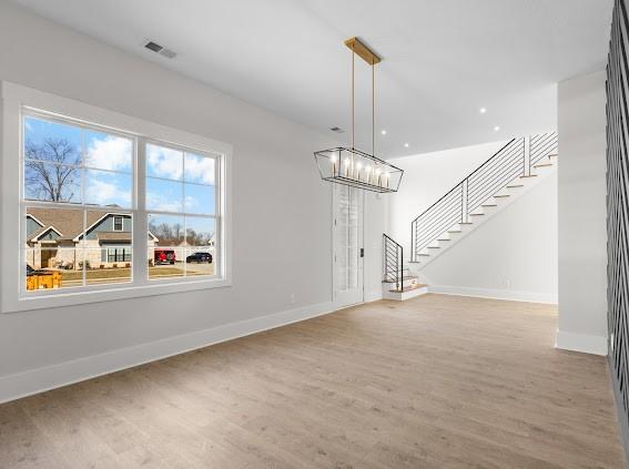 unfurnished dining area featuring stairs, a chandelier, wood finished floors, and baseboards