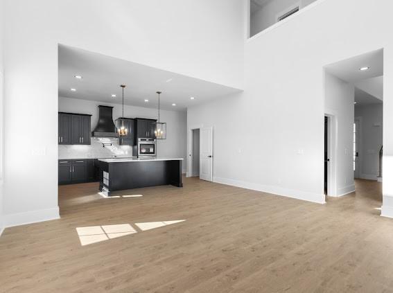 kitchen with open floor plan, a kitchen island with sink, light countertops, premium range hood, and stainless steel oven