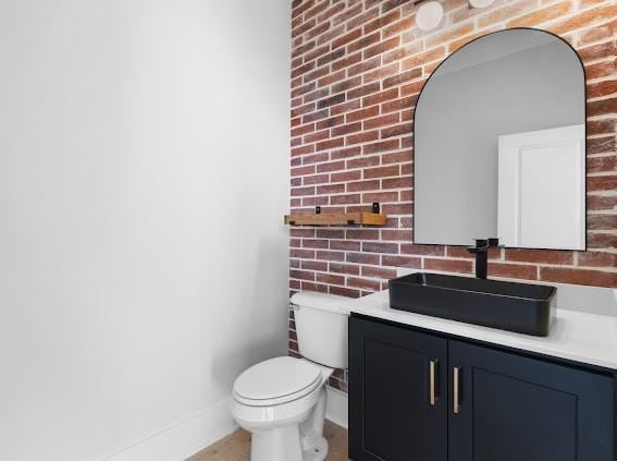 bathroom featuring baseboards, toilet, vanity, and brick wall