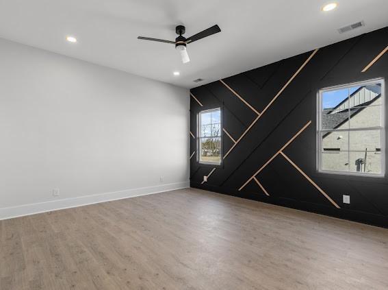 unfurnished room with ceiling fan, wood finished floors, visible vents, and baseboards