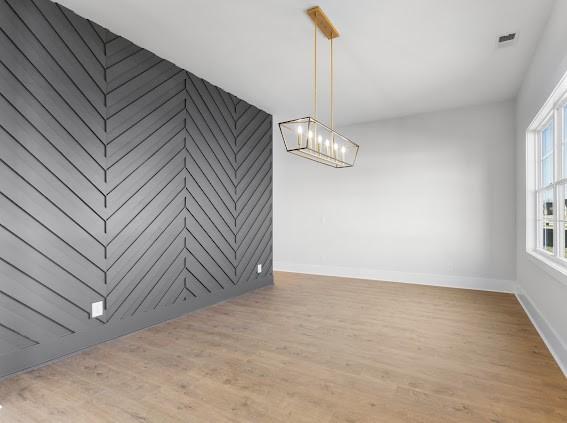 unfurnished room with a chandelier, an accent wall, wood finished floors, visible vents, and baseboards