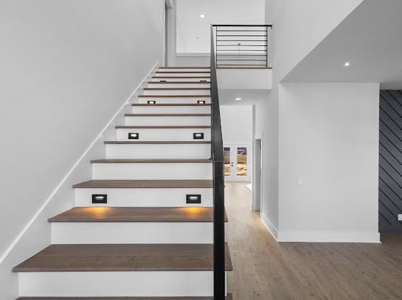 stairway with a high ceiling, baseboards, and wood finished floors