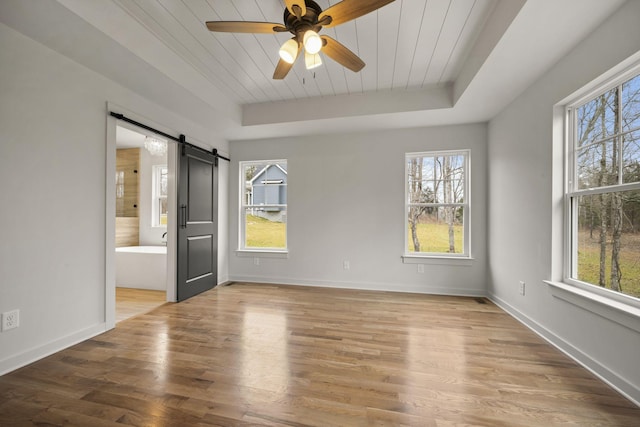 empty room with light hardwood / wood-style flooring, wooden ceiling, a barn door, and a raised ceiling