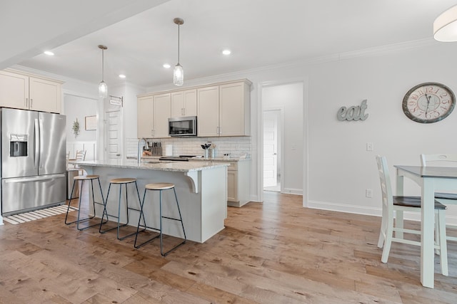 kitchen featuring a kitchen island with sink, backsplash, stainless steel appliances, light stone countertops, and decorative light fixtures