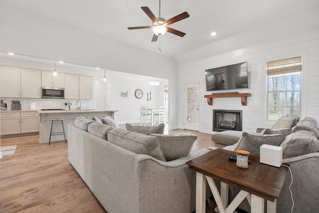 living room featuring vaulted ceiling, a large fireplace, sink, ceiling fan, and light hardwood / wood-style floors