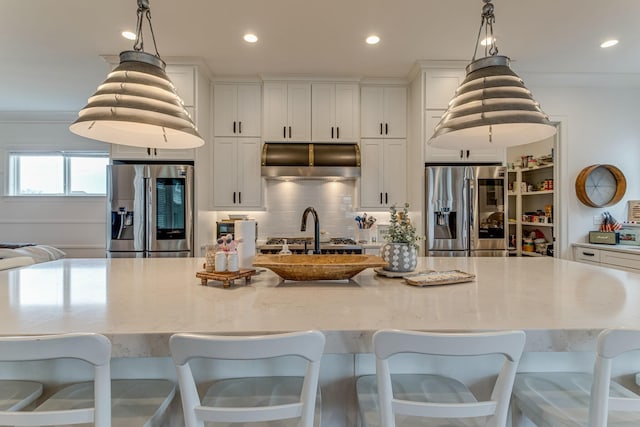 kitchen with hanging light fixtures, range hood, a large island with sink, and stainless steel fridge with ice dispenser