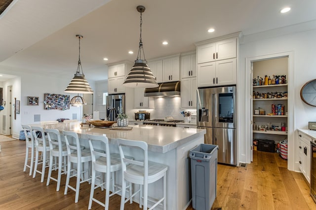 kitchen with white cabinets, hanging light fixtures, a large island with sink, and stainless steel refrigerator with ice dispenser