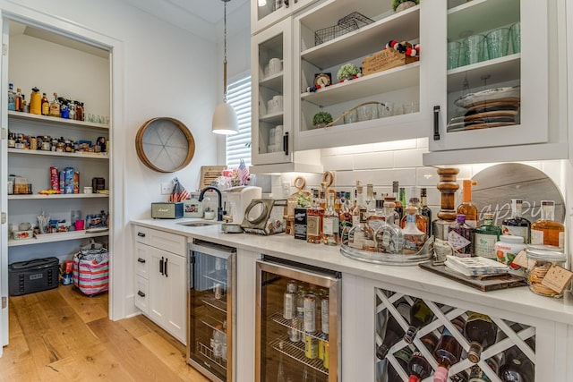 bar with sink, decorative light fixtures, beverage cooler, and white cabinets