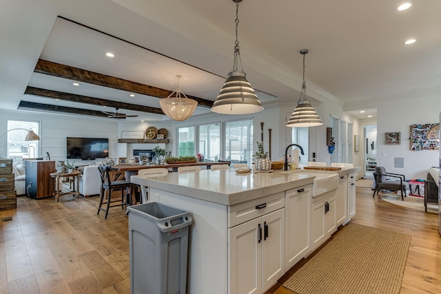 kitchen featuring pendant lighting, sink, a kitchen island with sink, light stone countertops, and white cabinets