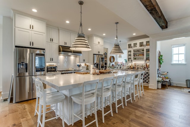 kitchen with a large island, stainless steel fridge, stainless steel refrigerator, white cabinetry, and hanging light fixtures