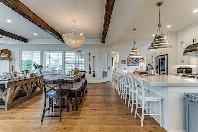 kitchen with stainless steel refrigerator with ice dispenser, light stone counters, decorative light fixtures, a large island with sink, and white cabinets