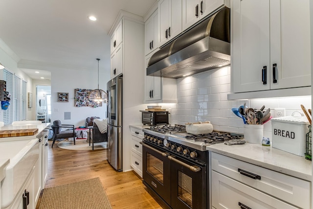 kitchen featuring stainless steel fridge, white cabinetry, double oven range, hanging light fixtures, and light wood-type flooring