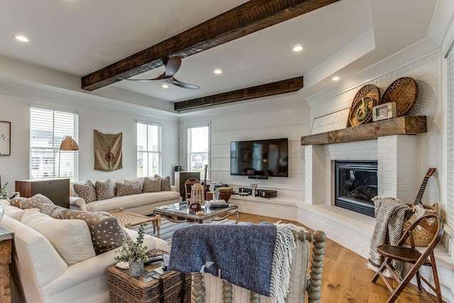 living room with beamed ceiling, ceiling fan, a fireplace, and light hardwood / wood-style floors