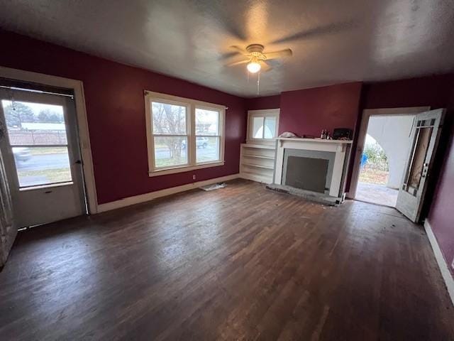 unfurnished living room with dark wood-type flooring, a brick fireplace, and a wealth of natural light