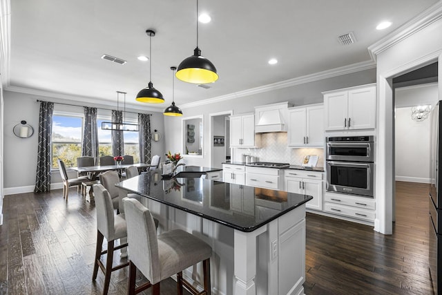 kitchen with white cabinets, backsplash, hanging light fixtures, a center island, and custom range hood