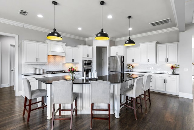 kitchen featuring premium range hood, appliances with stainless steel finishes, white cabinets, and decorative light fixtures