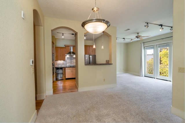 unfurnished living room featuring rail lighting, ceiling fan, a textured ceiling, light carpet, and beverage cooler