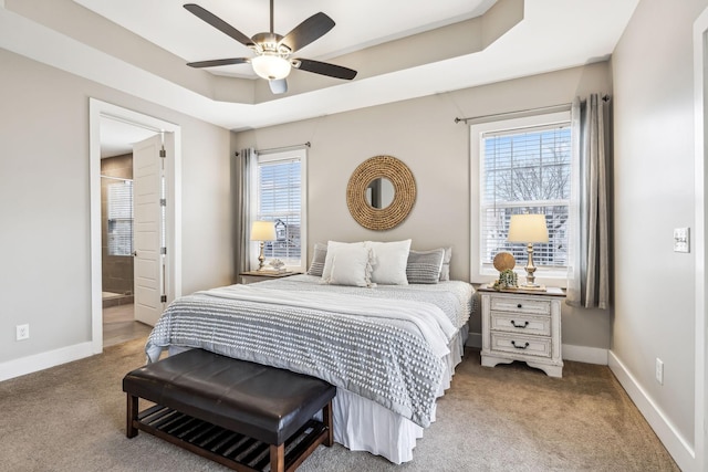 carpeted bedroom featuring multiple windows, connected bathroom, a raised ceiling, and ceiling fan