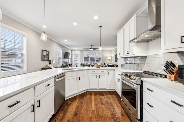 kitchen featuring hanging light fixtures, stainless steel appliances, white cabinets, and wall chimney exhaust hood