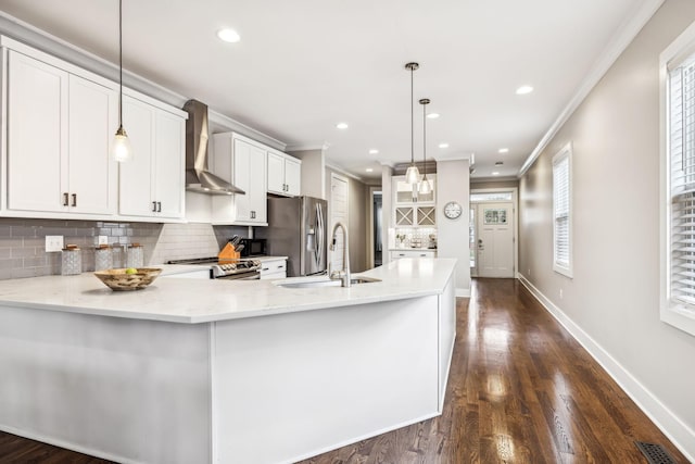 kitchen with crown molding, appliances with stainless steel finishes, pendant lighting, wall chimney range hood, and white cabinets