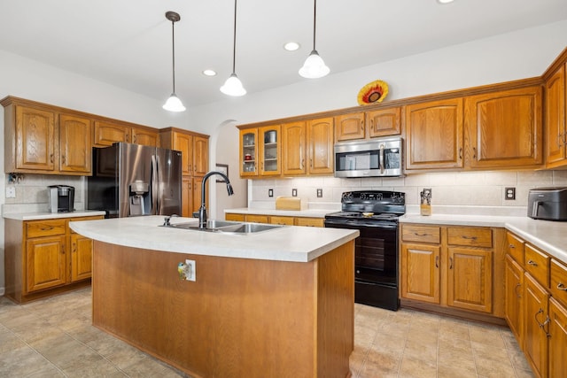 kitchen featuring decorative light fixtures, sink, backsplash, stainless steel appliances, and a center island with sink