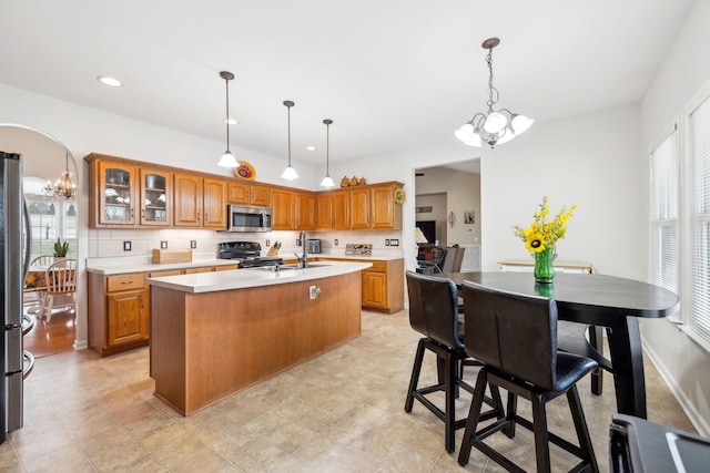 kitchen with appliances with stainless steel finishes, a kitchen island with sink, hanging light fixtures, backsplash, and an inviting chandelier