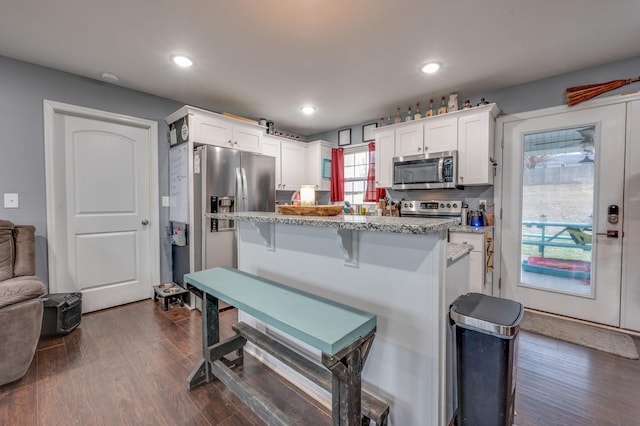 kitchen with a kitchen bar, white cabinetry, appliances with stainless steel finishes, dark hardwood / wood-style flooring, and light stone countertops