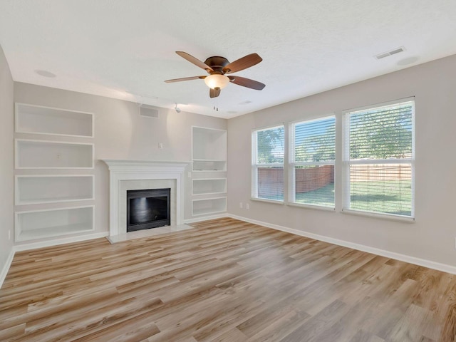 unfurnished living room with ceiling fan, a textured ceiling, built in features, and light hardwood / wood-style floors