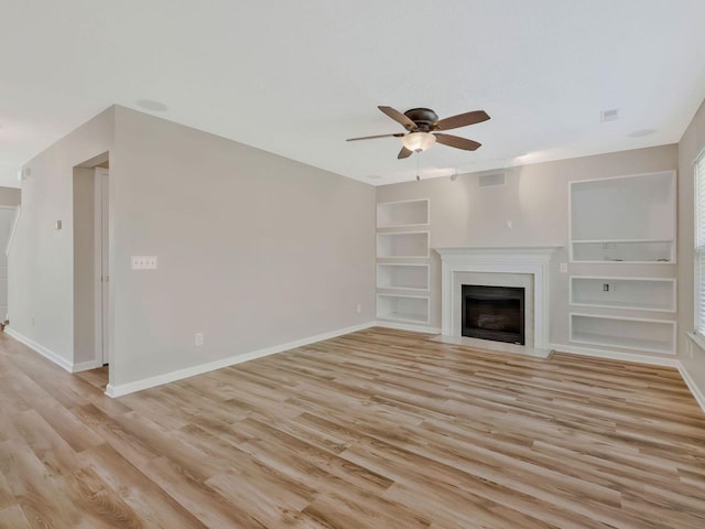 unfurnished living room featuring built in shelves, ceiling fan, and light wood-type flooring