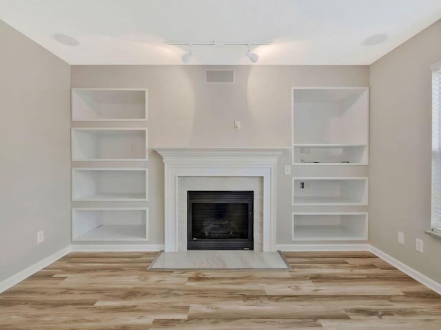 unfurnished living room with hardwood / wood-style flooring, a textured ceiling, built in features, and a high end fireplace